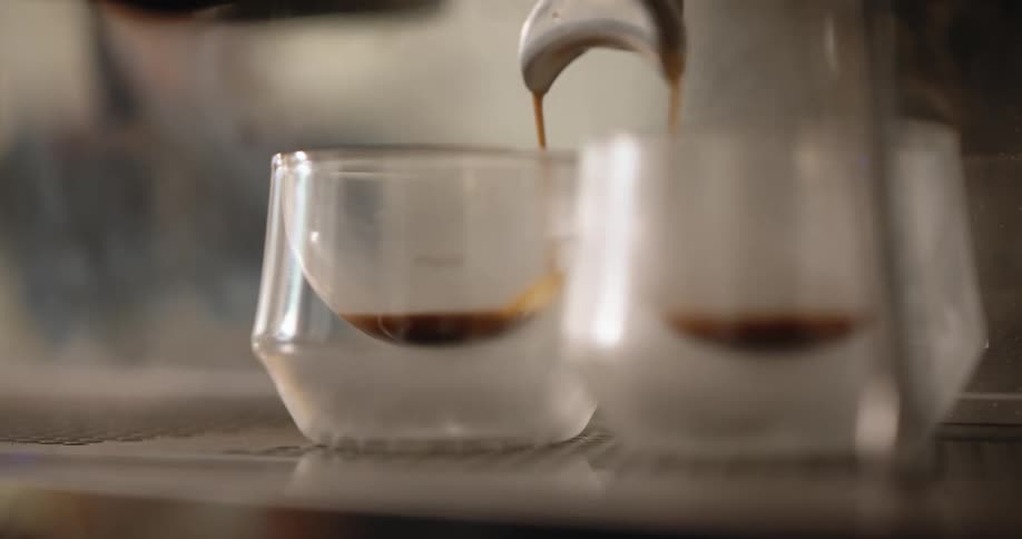 Expresso coffee is poured into two glasses from a machine