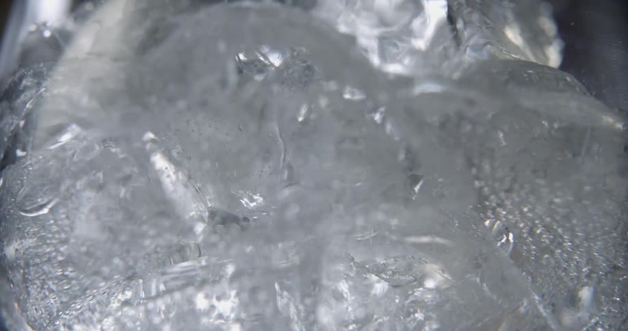 An extreme close up of bubbles rising up as a clear liquid is poured over ice.