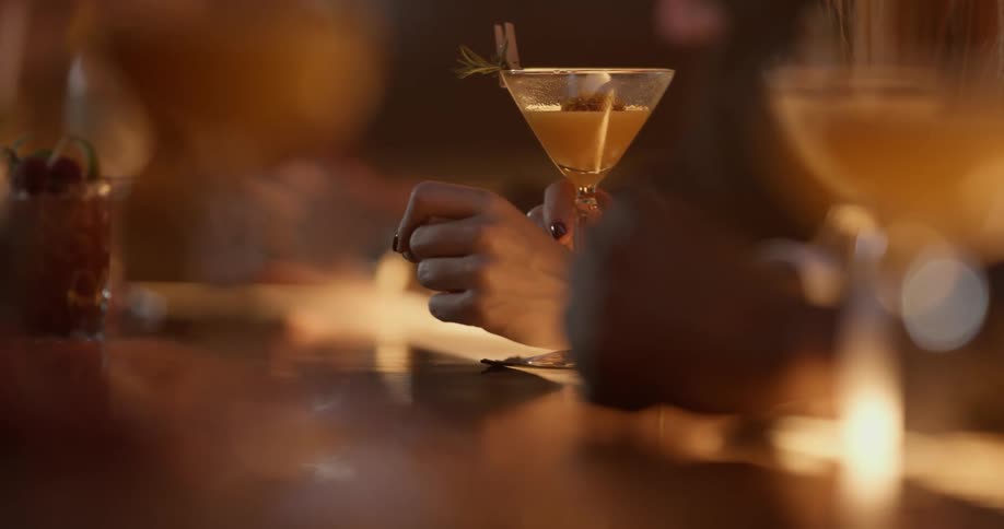 Looking across the bar, a woman holds the stem of her cocktail glass.