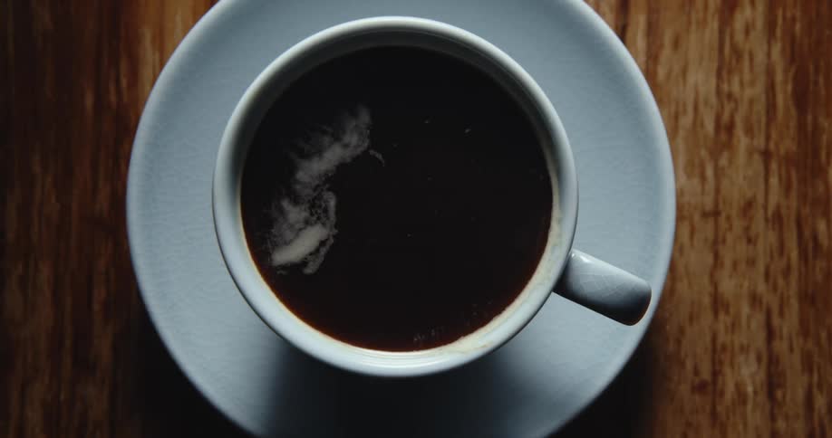Light moves across a top shot of a cup of black coffee