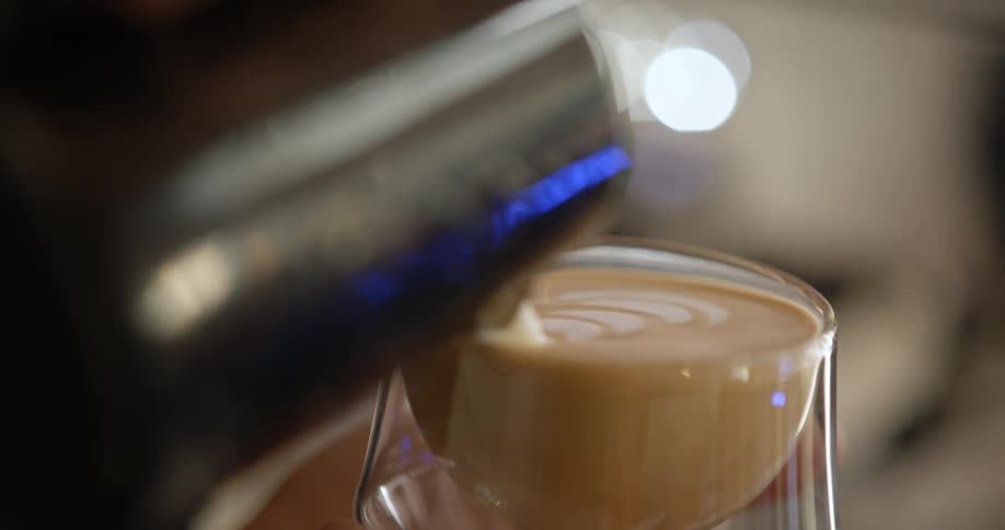 A woman pours hot milk into a cappuccino creating a fern design