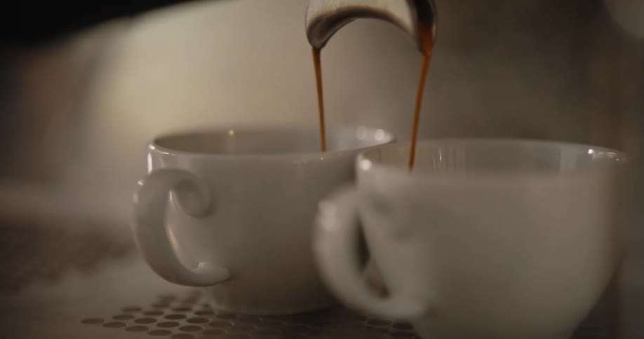 Expresso coffee pours from a machine into two cups
