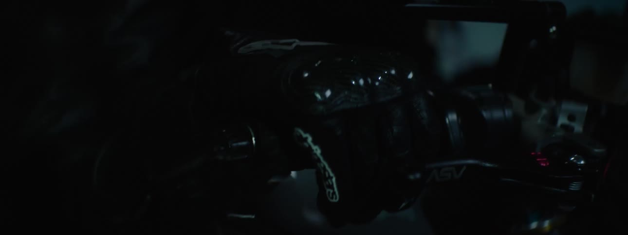 A person wearing a back leather jacket and a black helmet sits on a motorcycle as a strobe light flashes