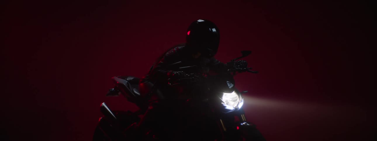 A woman sitting on a motorcycle puts down the visor on her helmet and turns on the headlight and holds the handlebars as she is ready to take off