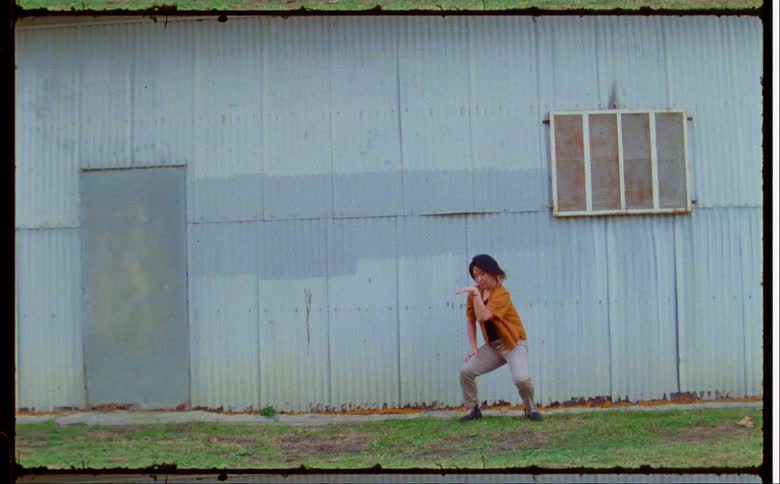 A teenage girl is standing outside of a building moving her arms as she dances