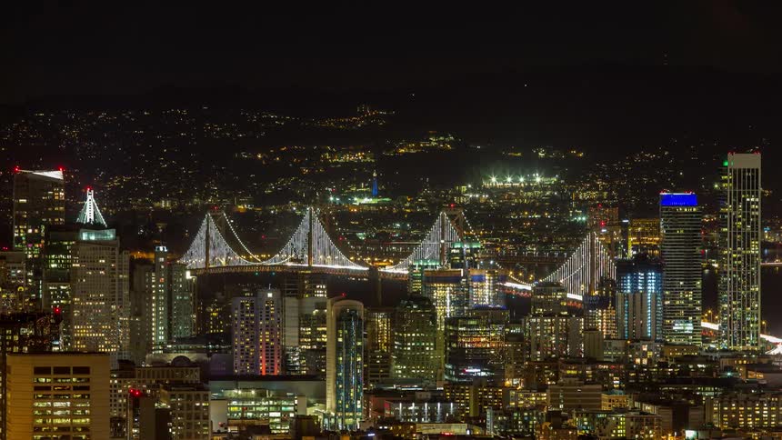 A time lapse shows an illuminated bridge with a stream of traffic crossing it