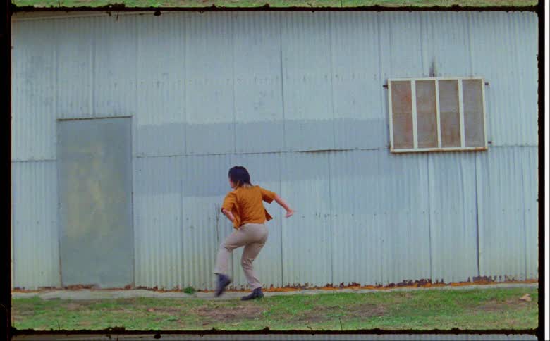 Dancer with orange shirt and beige pants dances in front of building