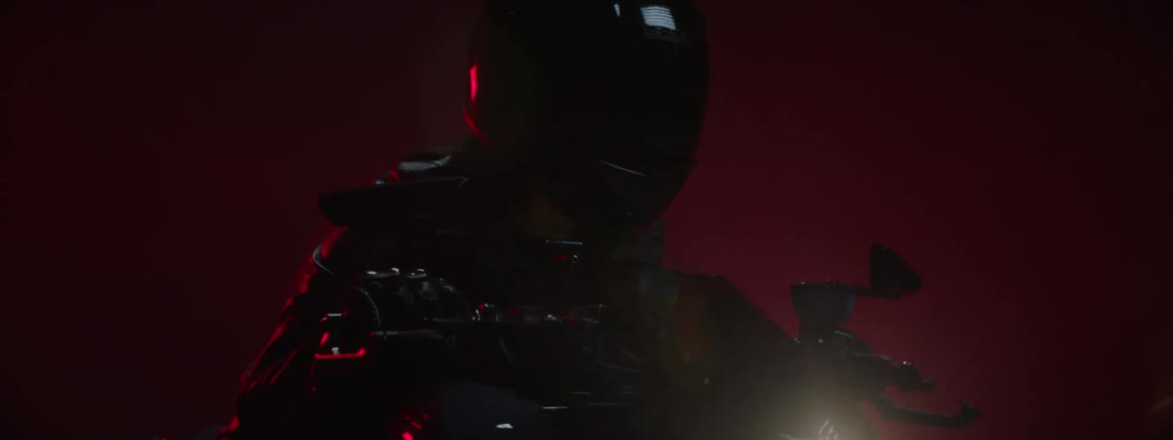 A person on a motorcycle with the headlights on in all black as they put their face shield down on their helmet