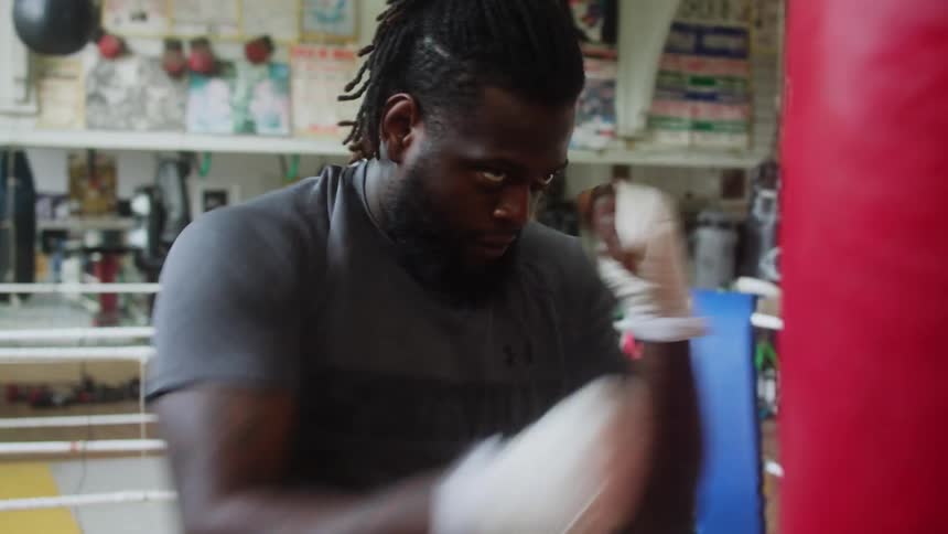 A man repeatedly punches a large punching bag inside of a boxing gym
