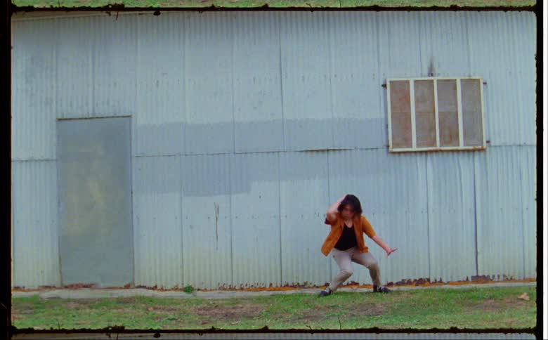 Woman dances on lawn outside corrugated metal building