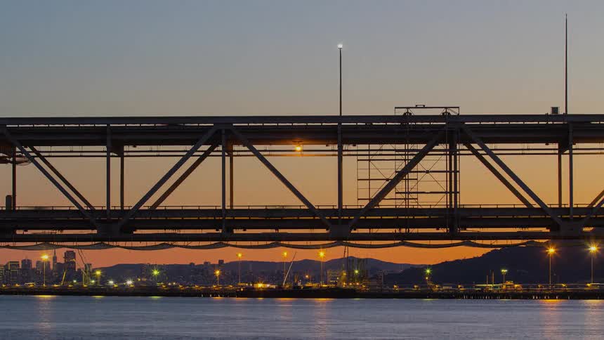 A time lapse shows the flow of traffic across a bridge as the sun is low in the sky