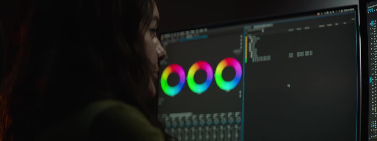 A woman is sitting at a desk as she looks at computer monitors