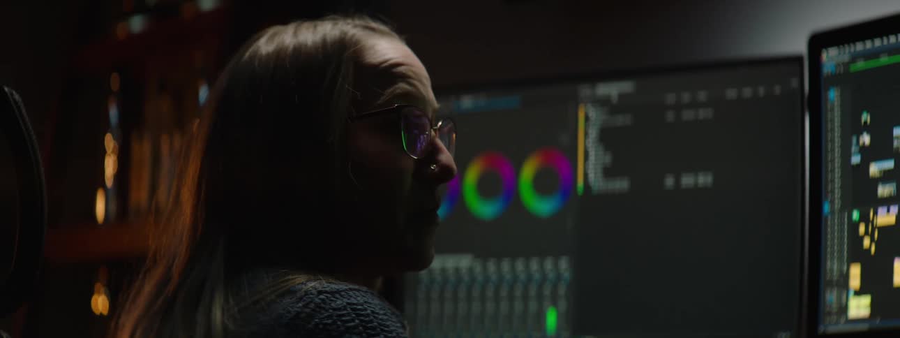A woman is sitting in front of two computer monitors