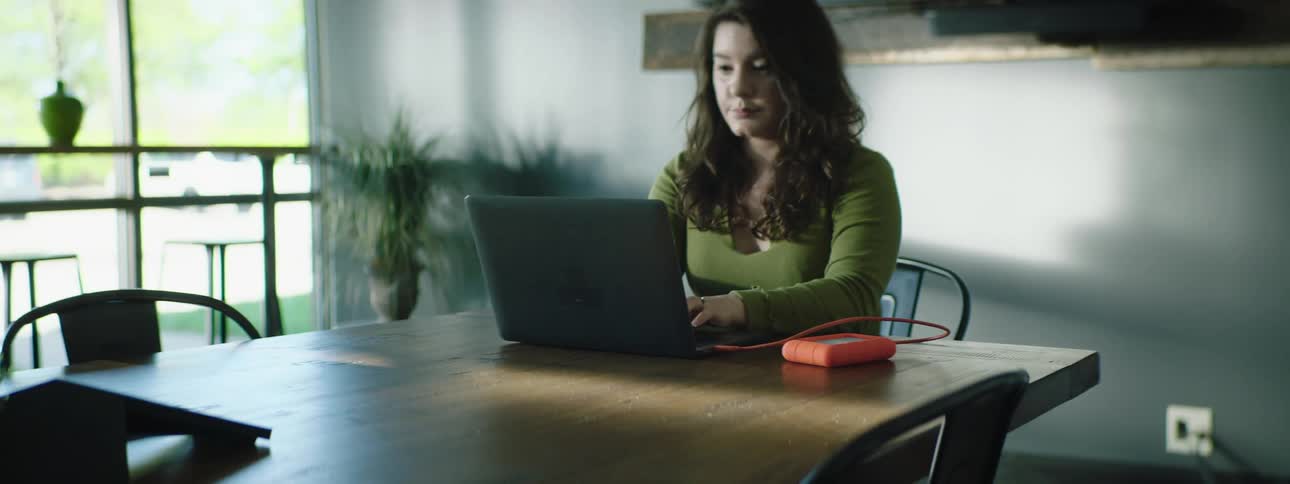 A woman sits at a dining table while typing on her laptop computer