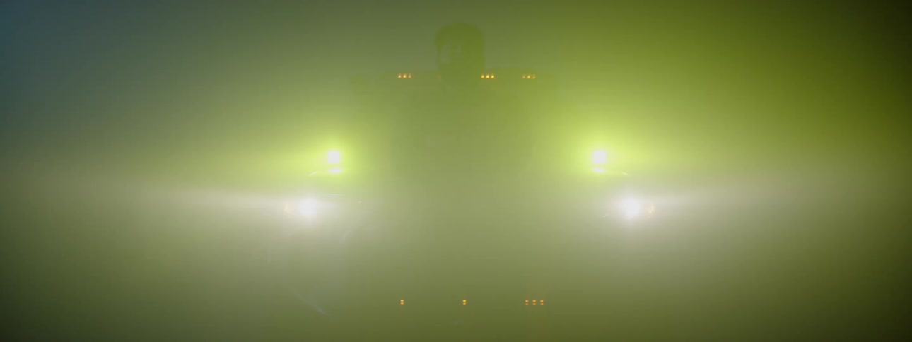 The silhouette of a man standing in front of a vehicle with head lights and a light bar on at night