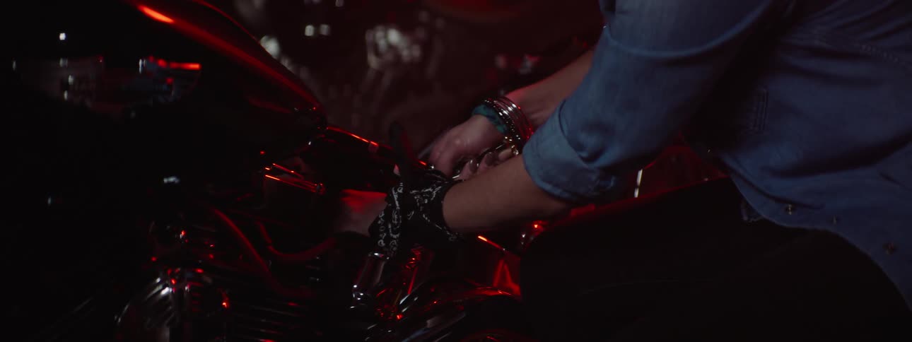 Young woman mechanic in a warehouse or garage at nighttime working on a motorcycle