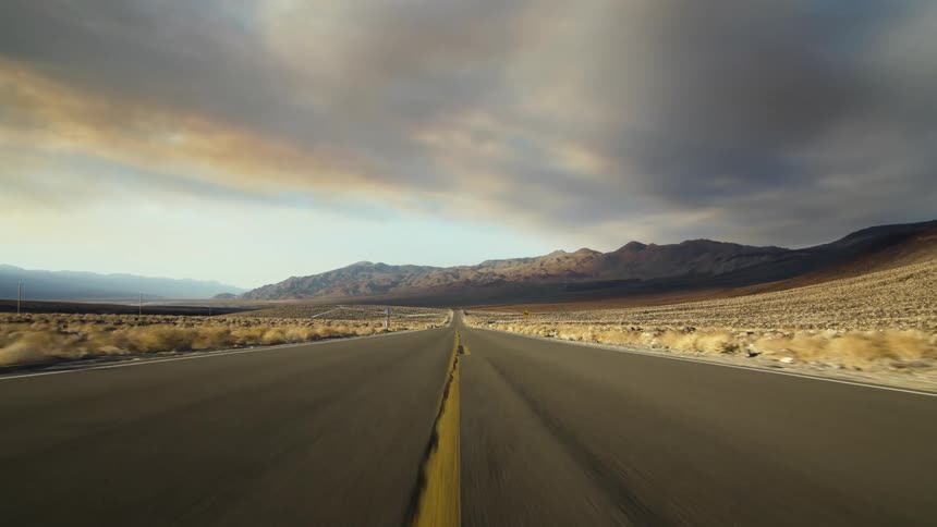 Highway passes through arid scrub land toward mountains under dark clouds