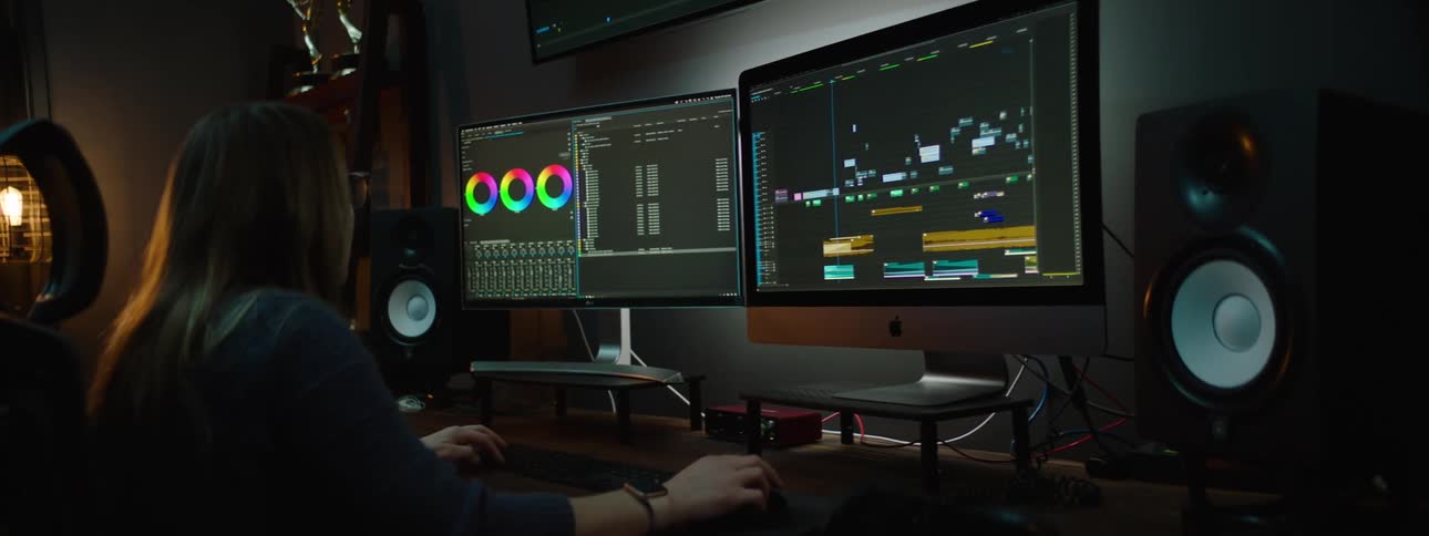 A woman sits at a desk while using software displayed across multiple screens