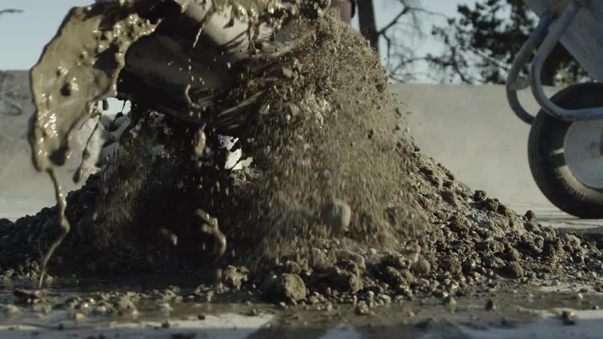 A close up of concrete mix being mixed with water by shovels wielded by two people