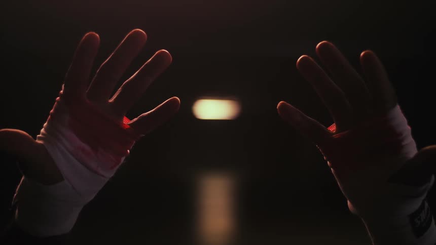A man turns his fists and opens his hands as they are wrapped in bloody gauze
