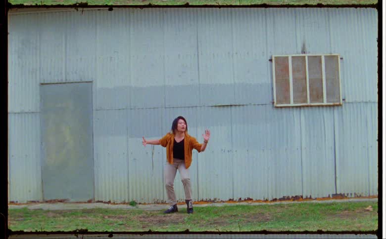 Woman dances in yard near corrugated metal building