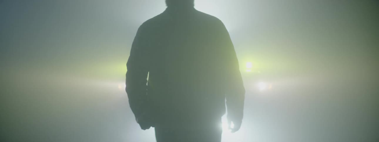 A mans silhouette in front of a vehicle with headlights on behind him
