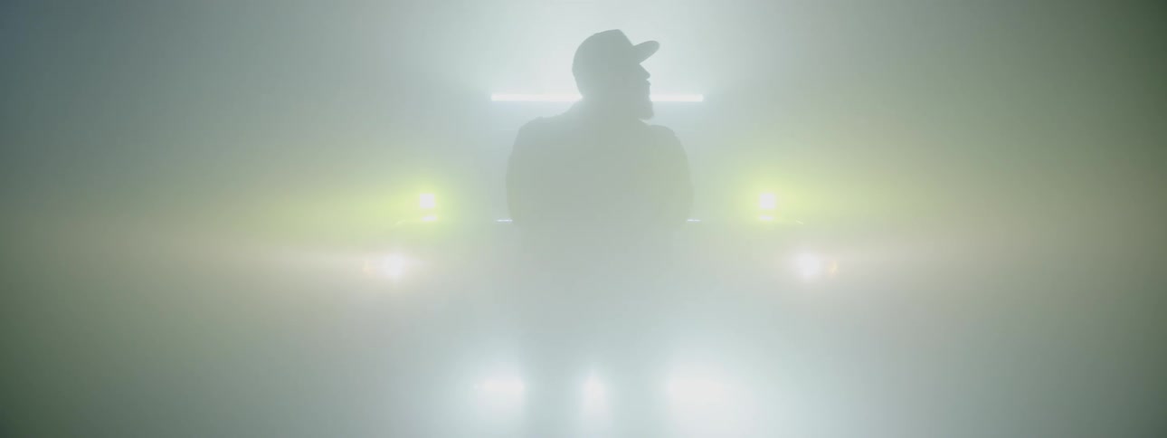 A man standing in front of a vehicle that turns on multiple head lights and a light bar creating a silhouette of the man