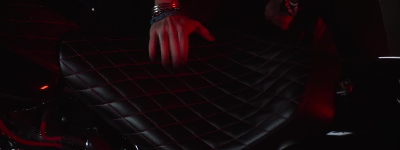 A woman with painted fingernails wearing bracelets and rings rubs the seat of a motorcycle