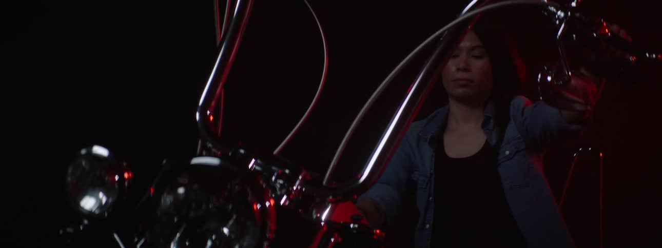 Woman sits on motorcycle in dark area lit by red lighting