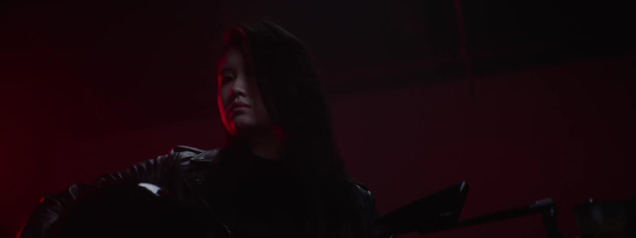 A woman wearing a black leather jacket holding her helmet while sitting on a black motorcycle