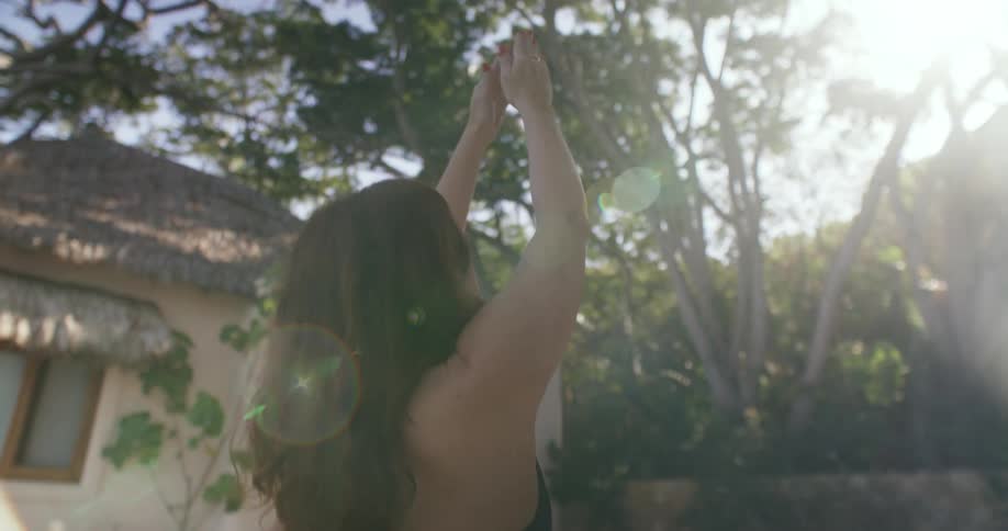 A woman reaches up while doing yoga in her backyard