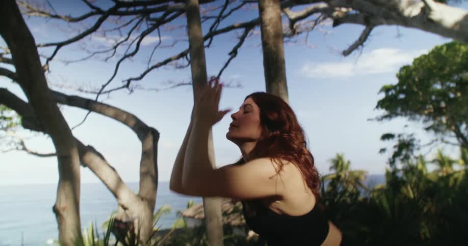 A woman stretching doing yoga outdoors with the ocean in the background
