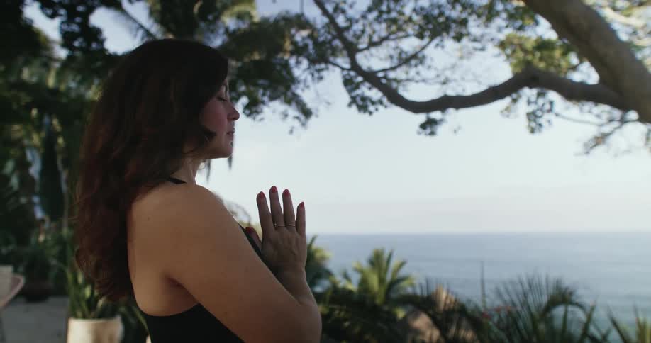 A woman is meditating outdoors in a tropical area