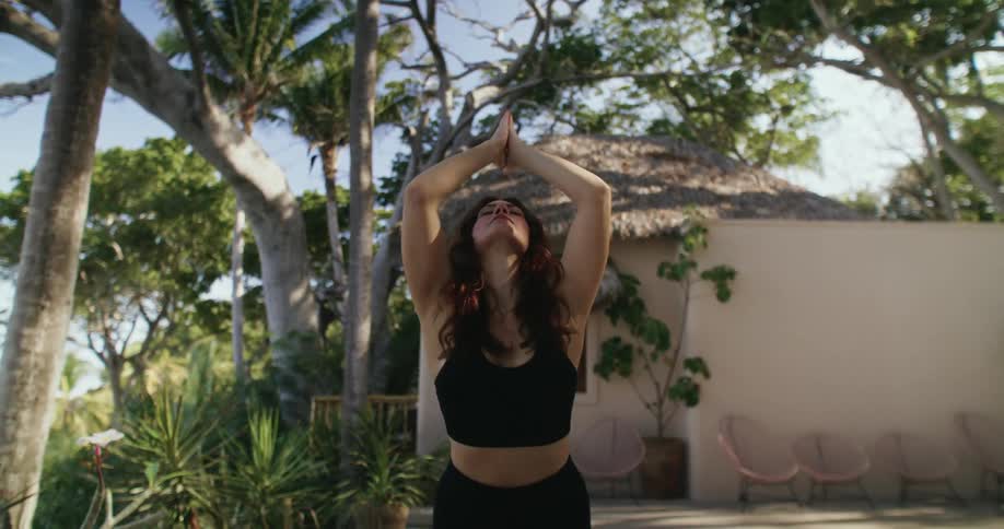 Woman with black top and pants does yoga on yoga mat in the backyard