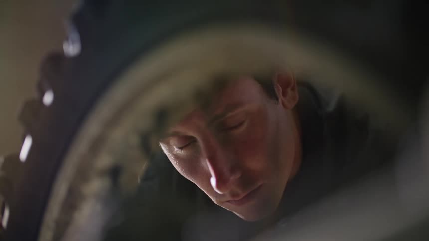 A close up of a bicycle tire and spoke as a man looks closely at it