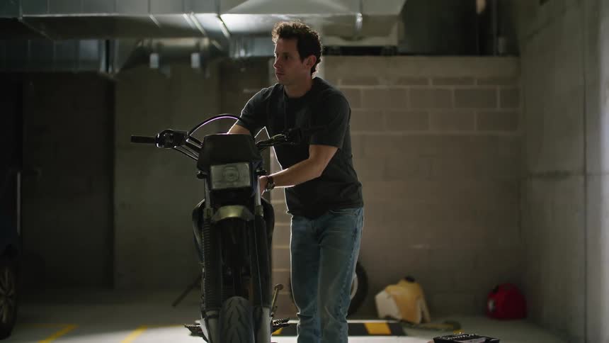 A man works on his scooter in a parking garage space