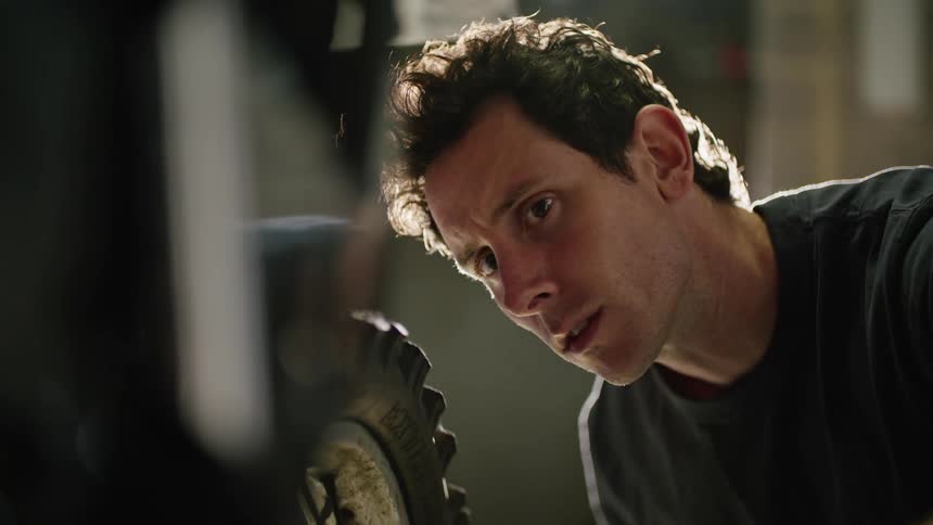 A man is looking forward as he turns the rear wheel of a motorcycle in a garage