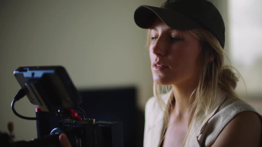 Man passes in the background as blonde woman operates professional video camera