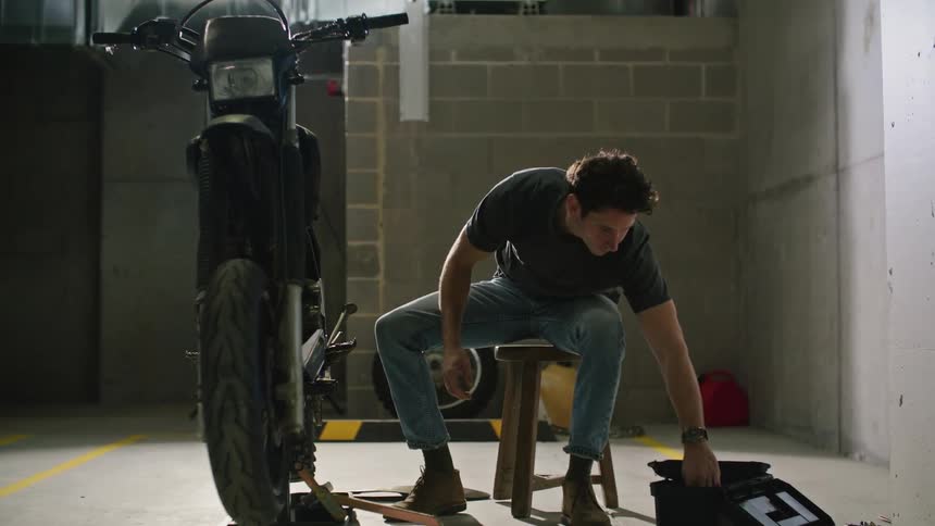 A man works on his motorcycle in a parking garage spot