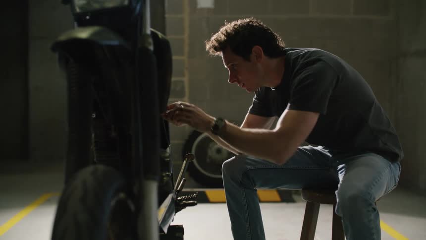 Man sits on stool working on motorcycle