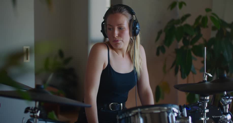 A woman playing a drum set with headphones on while she looks frustrated