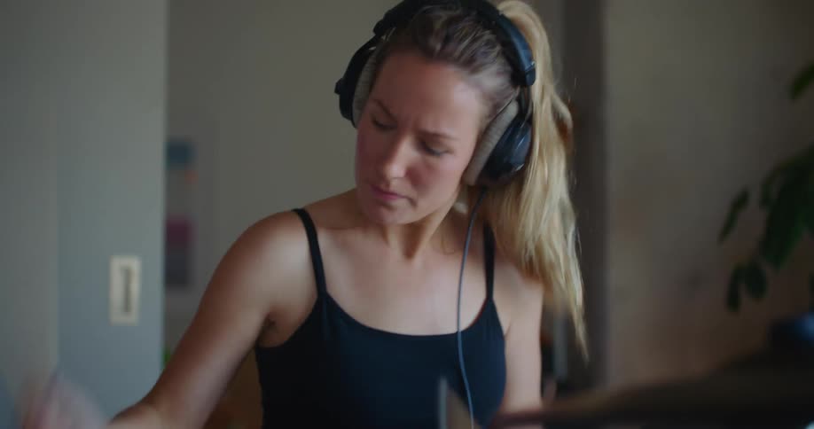 A woman playing a drum set wearing headphones and looking determined