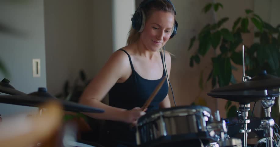 A woman playing drums wearing headphones smiling and enjoying herself