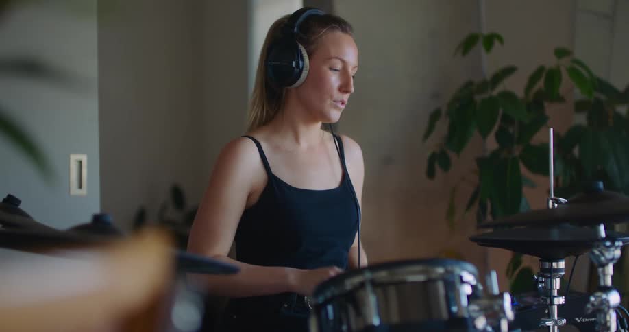 A woman wears headphones while playing the drums