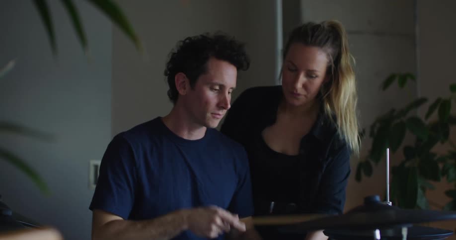 A woman teaches a man how to play the drums