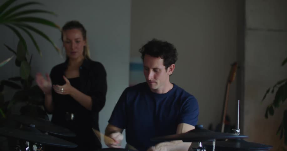 Female music teacher claps hands to keep beat and watches drumming student practice in studio