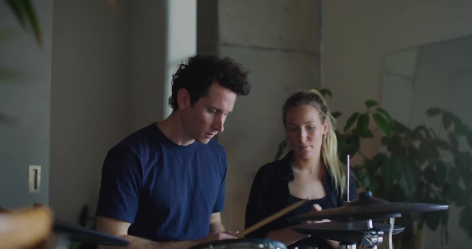 A woman teaches a man how to play the drums