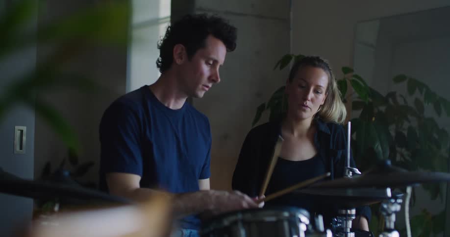 A man sitting in front of a drum set showing the woman sitting next to him how to play