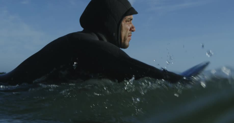 A man wearing a wetsuit is lying on a surfboard as he swims across the water