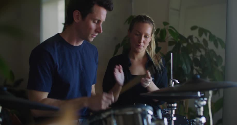 A man is holding drums sticks as the woman standing next to him moves her hands and claps as he plays